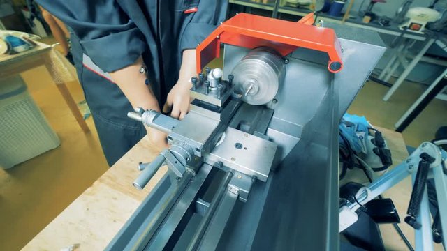 A man with prosthetic hands is working with a metal lathe in a factory equipment.