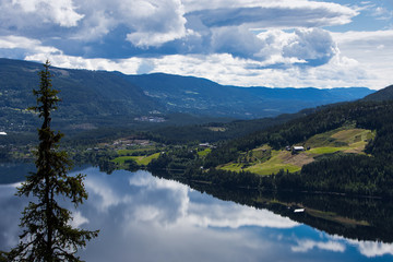 A landscape with  mountains and clouds reflecting in calm water.