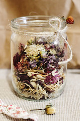 beautiful dried flowers, different flavors, in glass jar on rustic background of craft