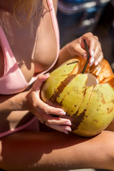 Surfer girl in sexy bikini drink coconut after have fun on big waves in open ocean with surf...