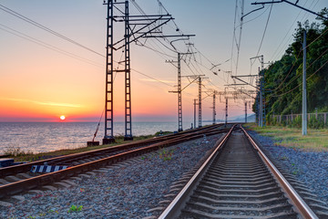 Naklejka na ściany i meble Beautiful landscape of a railroad and towers of traction line on the background of the sea at sunset, Sochi, Russia 