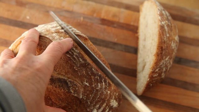 A woman has difficulty cutting through a loaf of tough-crusted bread