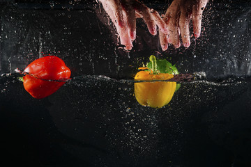 hand on top of several coloured paprika falling into water splash with many bubble