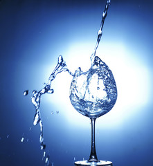 Pouring water into glass with water splashed out on blue background