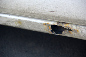 Large rusty hole in the threshold of a white passenger car