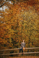 Outdoor portrait of beautiful woman enjoying autumn forest on a nice warm day, sitting on the fence