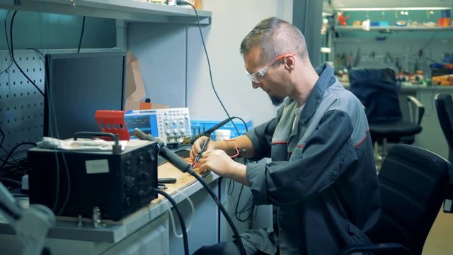 Workshop with a male employee soldering a circuit with artificial hands