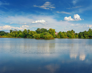 Tranquil landscape at a lake, with the vibrant sky, white clouds and the trees reflected