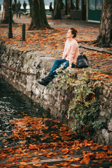 Lifestyle portrait of young woman resting by the lake on a nice and warm autumn day, wearing soft pullover and black boots. Image taken on lake Geneva, Lausanne, Switzerland