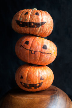 Halloween pumpkins with funny faces. Column of three pumpkins. Dark background.