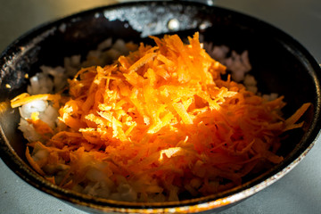 Grated carrots with onions in a skillet for frying