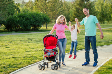 active happy family walking in summer park with a stroller with daughter