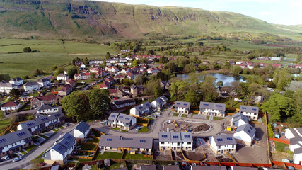 Low level aerial image over the rooftops of a rural housing estate with picturesque village pond. 