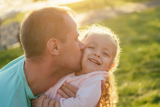 close-up portrait of father kissing happy little girl on cheek in summer park