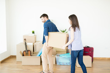 Fototapeta na wymiar Woman Assisting Man Carrying Heavy Box While Moving House