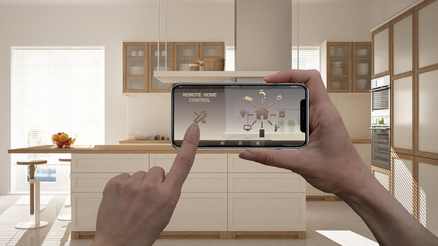 Remote home control system on a digital smart phone tablet. Device with app icons. Interior of minimalist white kitchen in the background, architecture design
