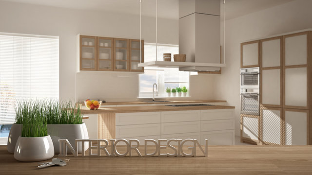 Wooden table, desk or shelf with potted grass plant, house keys and 3D letters making the words interior design, over blurred modern kitchen, project concept copy space background