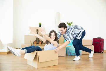 Man Pushing Woman Sitting In Cardboard Box In New Home