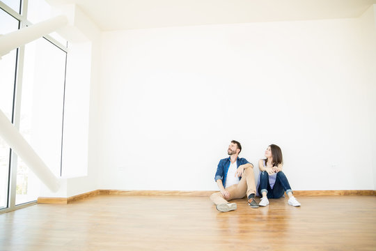 Couple Looking Away While Sitting Against Wall In New Apartment