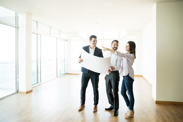 Happy Woman Pointing By Man And Agent In New Home