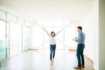 Man Looking At Excited Woman With Arms Raised In New House