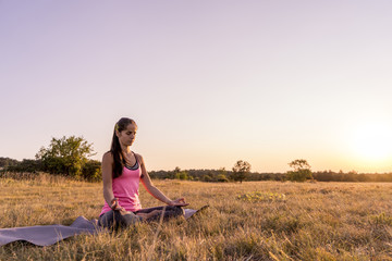 Young beautiful woman practicing Yoga outdoor in nature during sunset