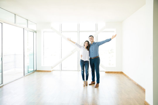 Smiling Couple Standing Arms Outstretched In New Apartment
