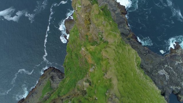 AERIAL, TOP DOWN, COPY SPACE: Unrecognizable female tourist hiking in picturesque Faroe Islands taking photos from the edge of a grassy cliff. Flying over a breathtaking abyss and deep blue ocean.