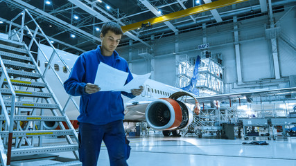 Aircraft maintenance mechanic in blue uniform is going down the stairs while reading papers in a...