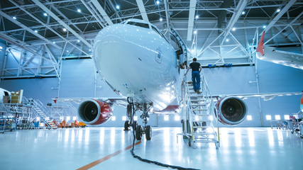 Obraz premium Fabrycznie nowy samolot w hangarze obsługi technicznej statku powietrznego, podczas gdy inżynier / technik / mechanik obsługi statku powietrznego wchodzi do kabiny przez drabinę / rampę.