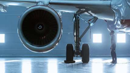 In a Hangar Aircraft Maintenance Engineer/ Technician/ Mechanic Visually Inspects Airplane's Jet...