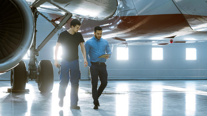 In a Hangar Aircraft Maintenance Engineer Shows  Technical Data on Tablet Computer to Airplane...