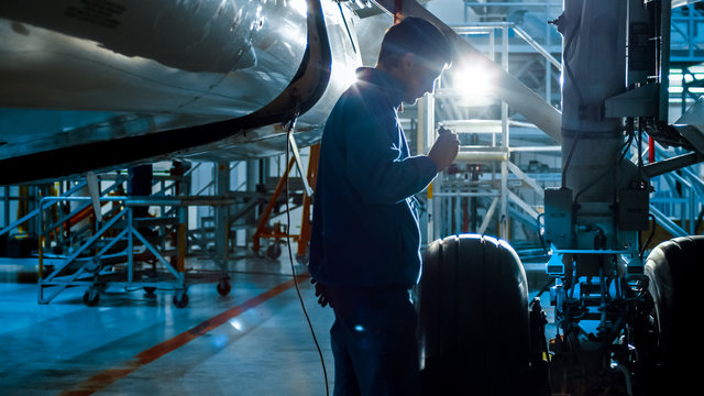 Aircraft maintenance mechanic with a flash light inspects plane chassis in a hangar.