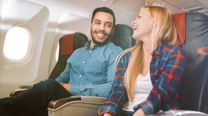 Obraz premium Na komercyjnym locie samolotem Przystojny Hiszpanin opowiada zabawną historię swojej pięknej blondynce. Oboje się śmieją. Podróżują w nowym samolocie z Sun Shining Through the Window.