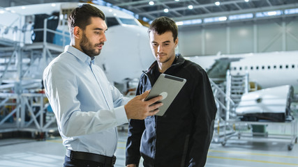Fototapeta na wymiar Aircraft Maintenance Worker and Engineer having Conversation. Holding Tablet.