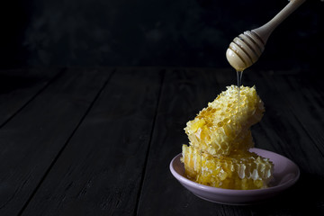 pieces of fresh honeycomb with a wooden dipper dripping honey on a ceramic plate on a slate...