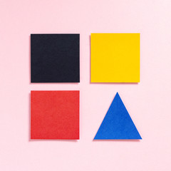Paper multicolored squares and a triangle on a pink background, top view. Geometric figures