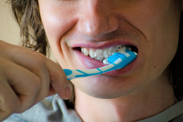 Close-up of a young man while brushing his teeth, personal hygiene. Young man brushing his teeth indoors.