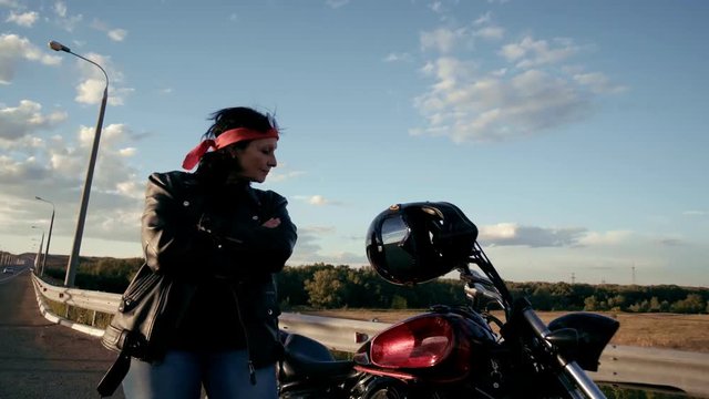 An old woman biker in a leather jacket and gloves comes to his motorcycle, turns to face the camera. A smiling woman can be seen from different sides. The life of an elderly rocker and biker after