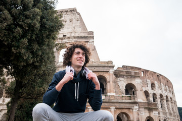 Handsome young sportsman relaxing after training with a towel around his neck in front of Colosseum...