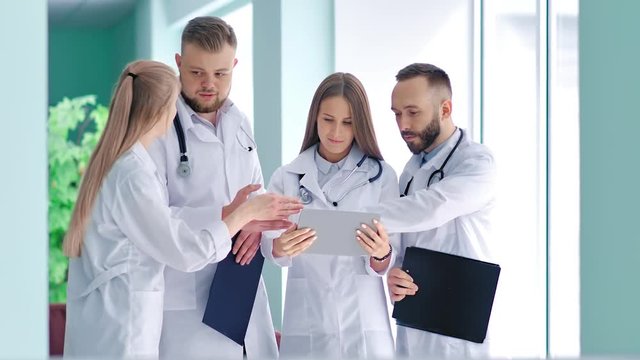 Group of young doctors with stethoscope discussing something looking at screen of tablet PC
