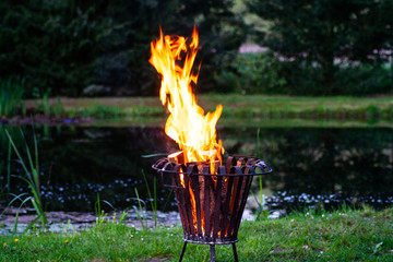 Flammen aus einem Feuerkorb am Gartenteich