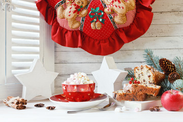  Cup of hot drink with marshmallow and Christmas cupcake. Composition with Christmas wreath, fur-tree branches and Christmas decorations. Close up on white vintage window with wooden shutters. 