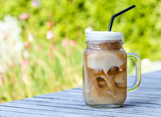 Ice coffee in glass mug with milk and cinnamon on wooden table in the garden.