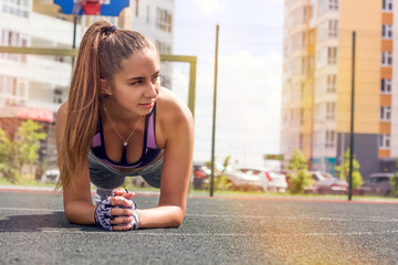 portrait of a young caucasian woman, tanned skin, slender body, doing planking exercise  on the street, sunny toned ,copy space