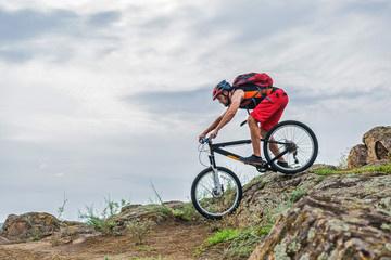 Plakat Cyclist in a helmet and with a backpack riding down the rock on a mountain bike, an active lifestyle.