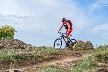Naklejka na ściany i meble Cyclist riding a mountain bike on rocks on the blue sky background.