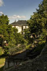Obraz premium Stadtvilla bei strahlendem Sonnenschein an einem Park mit vielen Bäumen und alter Stadtmauer, City villa in bright sunshine at a park with many trees and old city walls