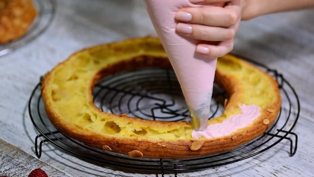 Half of a Paris Brest cake. Background: a pastry bag filling with whipped cream.