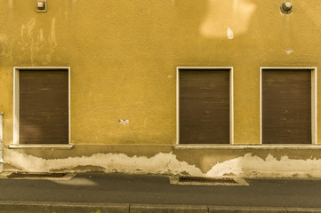 alte Fassade mit 3 braunen Rollladen aus Holz eines Hauses mit Gehsteig, old facade with 3 brown wooden shutters of a house with sidewalk